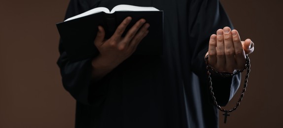 Photo of Priest with Holy Bible and rosary on brown background, closeup