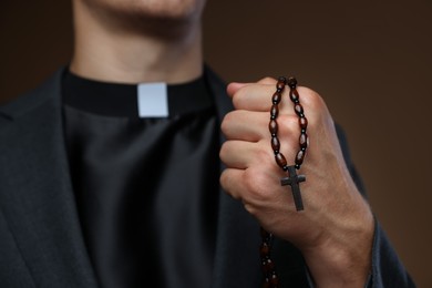 Photo of Priest with rosary on brown background, closeup