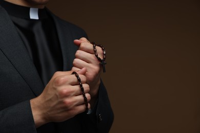 Photo of Priest with rosary on brown background, closeup. Space for text