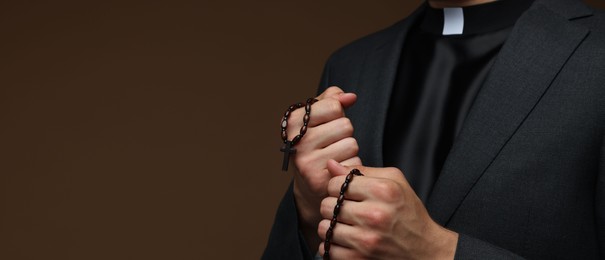 Photo of Priest with rosary on brown background, closeup. Space for text