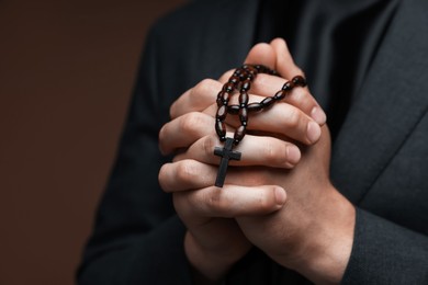 Photo of Priest with rosary praying on brown background, closeup