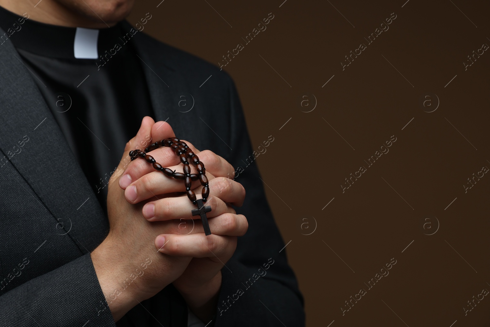 Photo of Priest with rosary praying on brown background, closeup. Space for text
