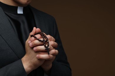 Photo of Priest with rosary praying on brown background, closeup. Space for text