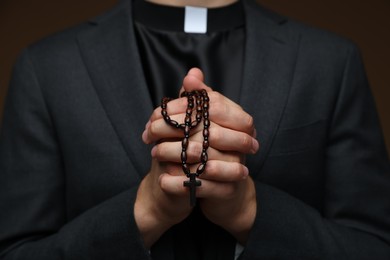 Photo of Priest with rosary praying on brown background, closeup