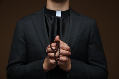 Photo of Priest with rosary praying on brown background, closeup