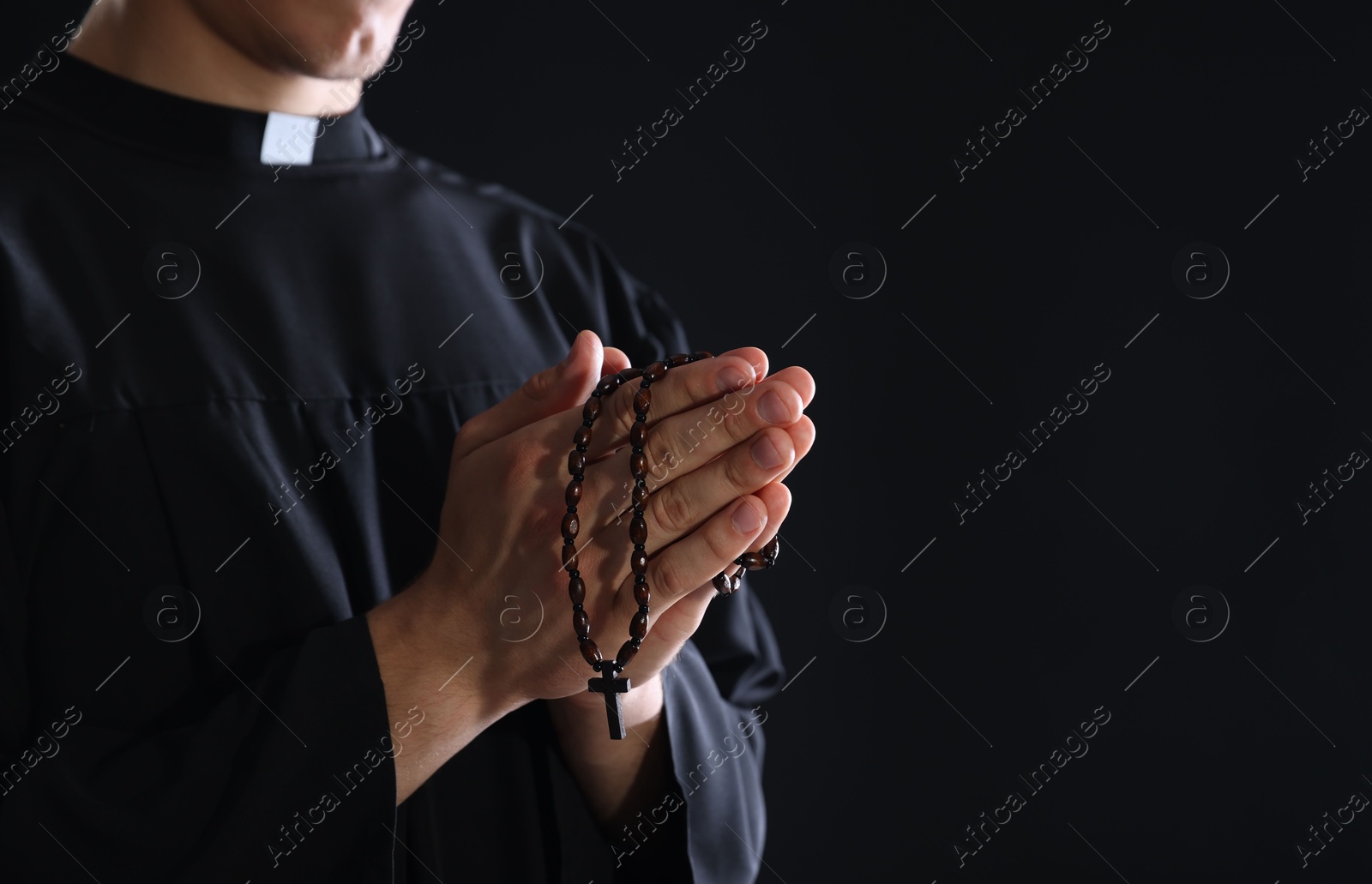 Photo of Priest with rosary praying on black background, closeup. Space for text