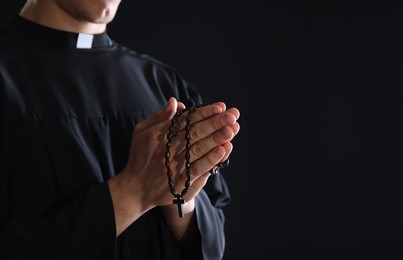 Photo of Priest with rosary praying on black background, closeup. Space for text