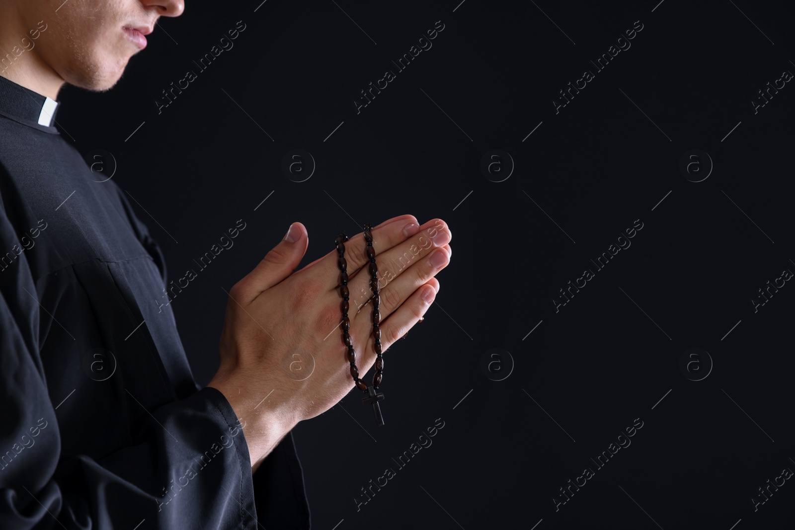 Photo of Priest with rosary praying on black background, closeup. Space for text