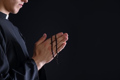 Photo of Priest with rosary praying on black background, closeup. Space for text