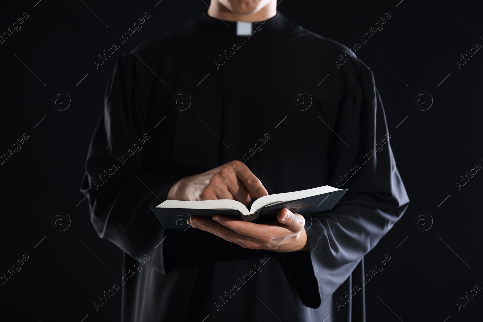 Photo of Priest with Holy Bible on black background, closeup