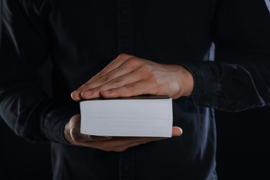 Photo of Priest with Holy Bible on black background, closeup