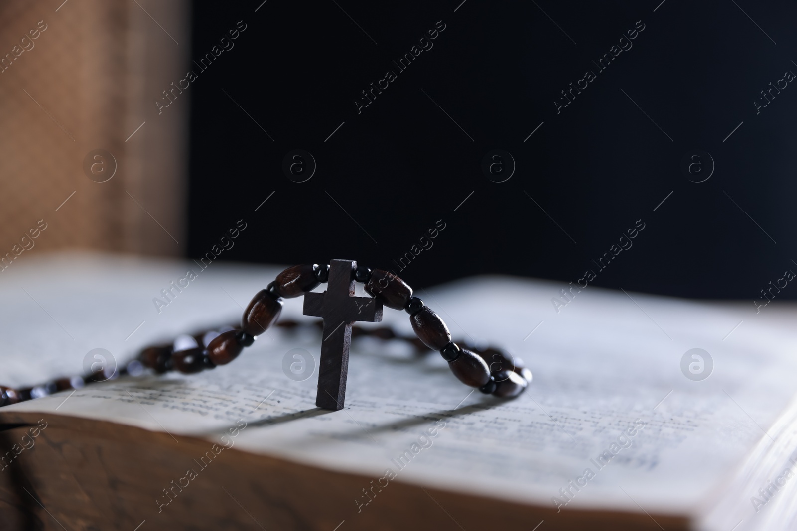 Photo of Rosary with wooden cross on Holy Bible against blurred background, closeup