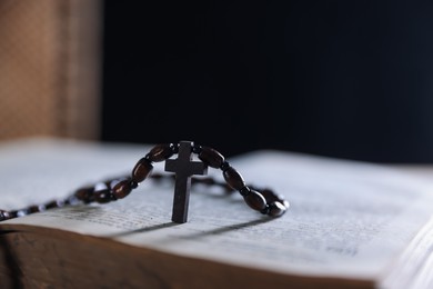Photo of Rosary with wooden cross on Holy Bible against blurred background, closeup