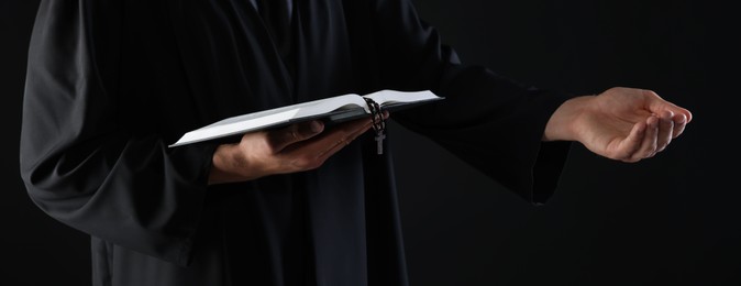 Photo of Priest with Holy Bible and rosary preaching on black background, closeup