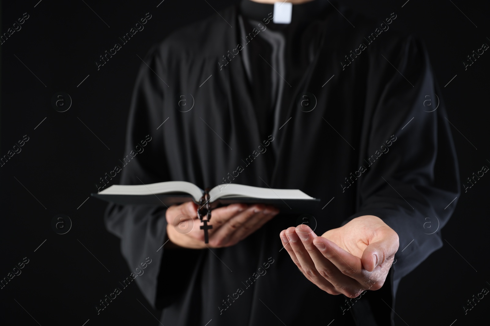 Photo of Priest with Holy Bible and rosary preaching on black background, closeup