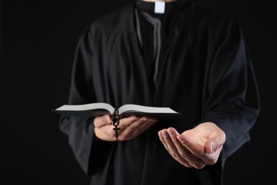 Photo of Priest with Holy Bible and rosary preaching on black background, closeup