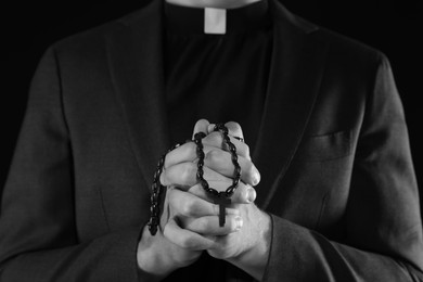Photo of Priest with rosary praying on dark background, closeup. Black and white effect