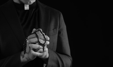 Photo of Priest with rosary praying on dark background, closeup. Black and white effect