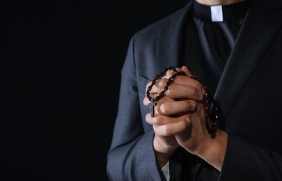 Photo of Priest with rosary praying on black background, closeup. Space for text