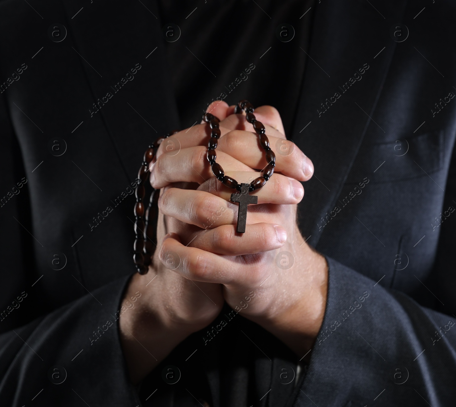 Photo of Priest with rosary praying on black background, closeup