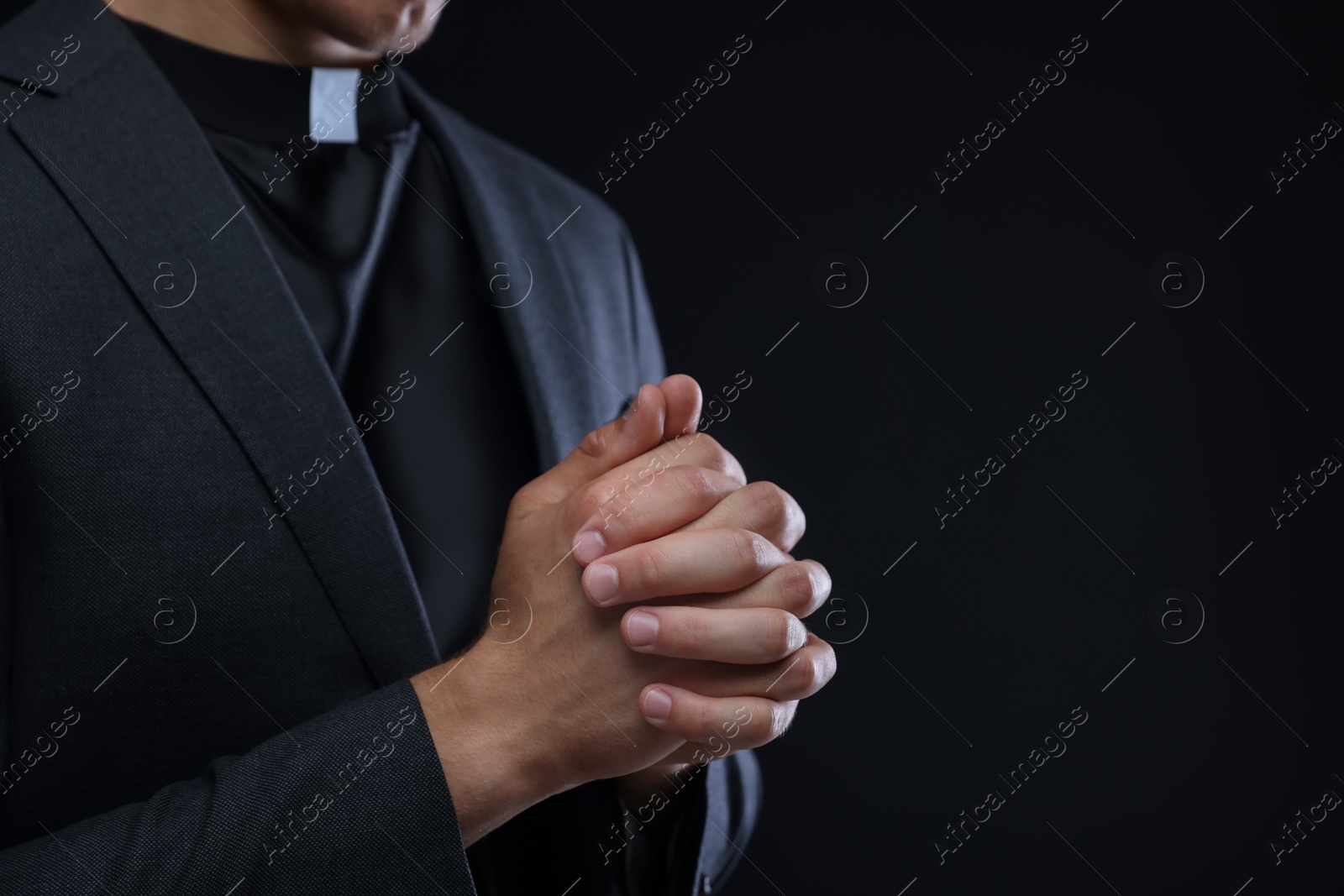 Photo of Priest praying on black background, closeup. Space for text