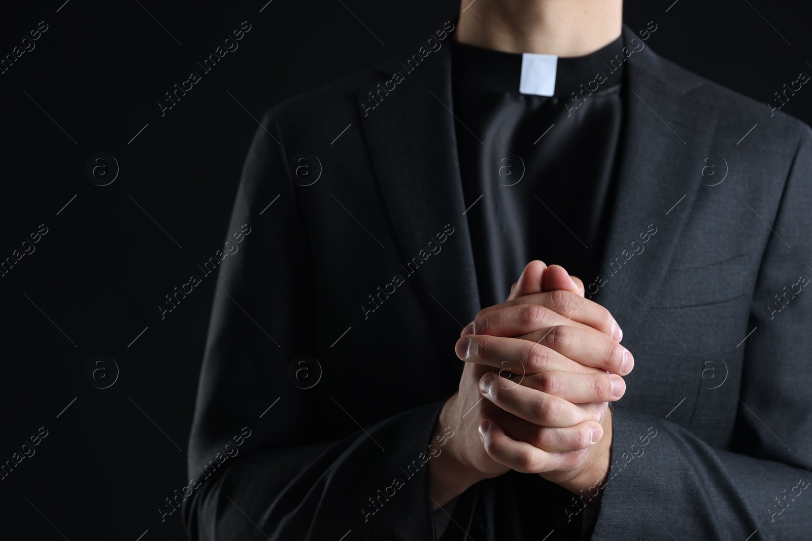Photo of Priest praying on black background, closeup view