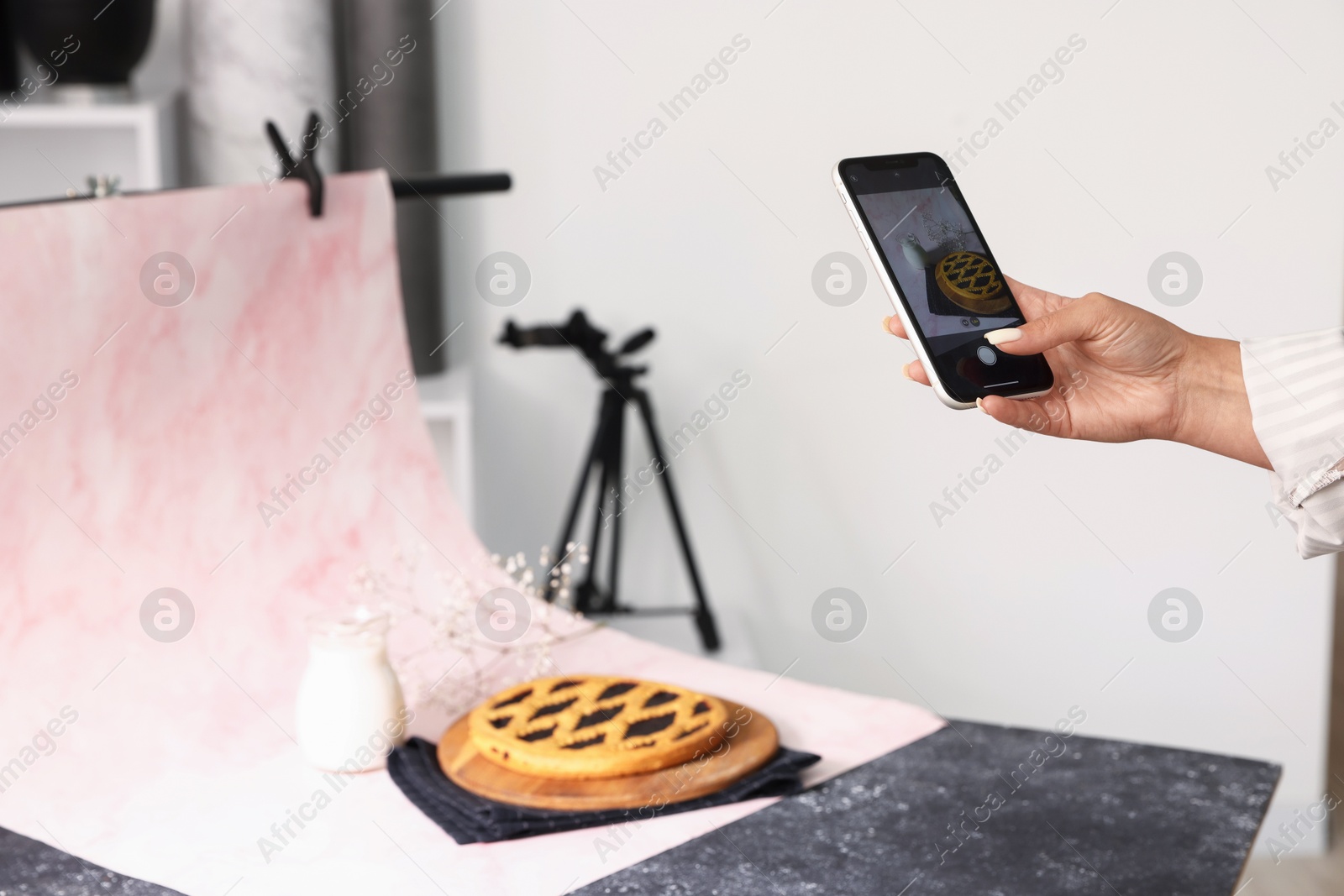 Photo of Woman taking picture of tasty pie and milk in studio, selective focus. Professional food photography