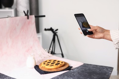 Photo of Woman taking picture of tasty pie and milk in studio, selective focus. Professional food photography