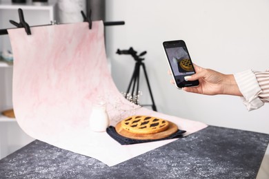 Photo of Woman taking picture of tasty pie and milk in studio, selective focus. Professional food photography