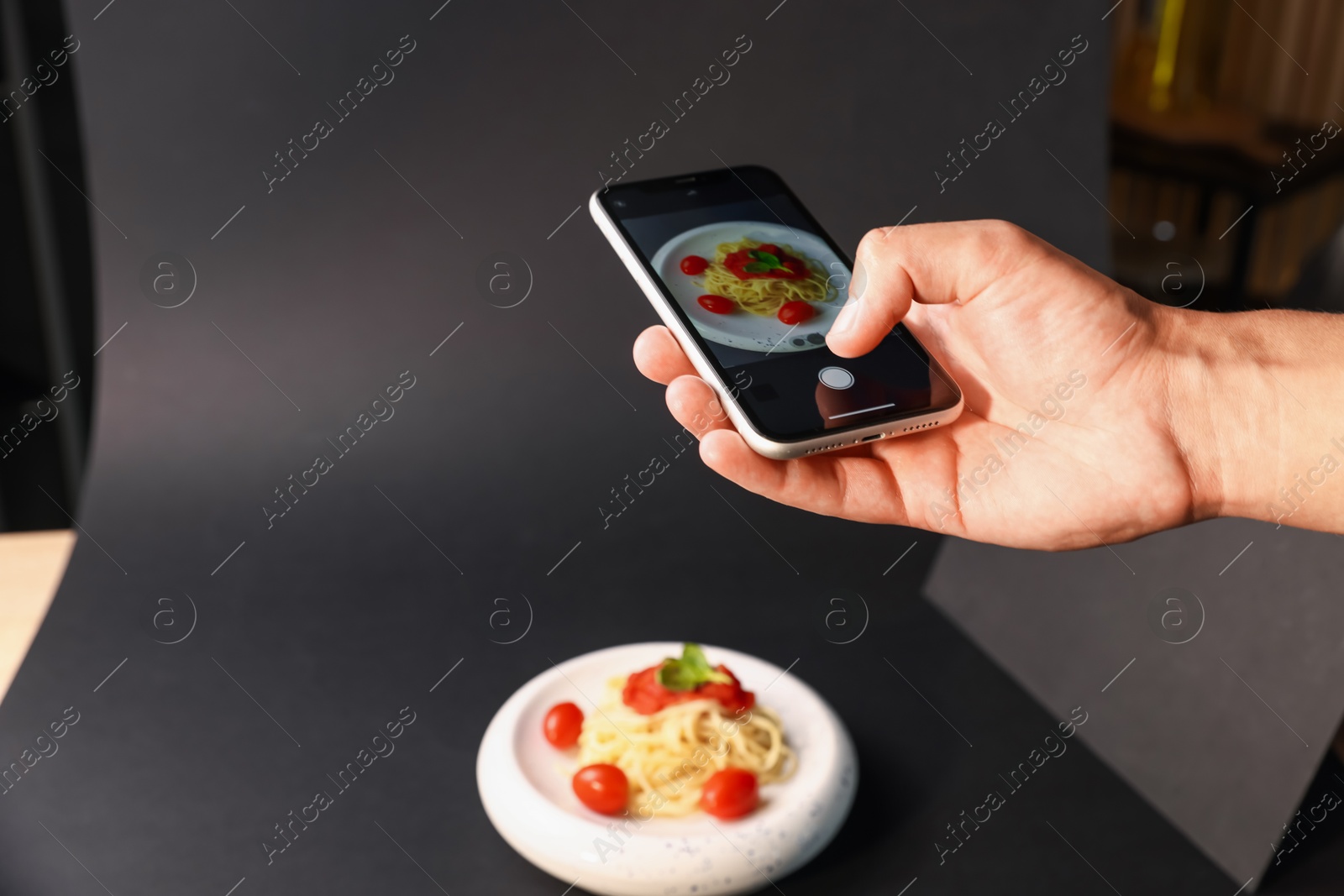 Photo of Man taking picture of pasta with smartphone in studio, closeup. Professional food photography