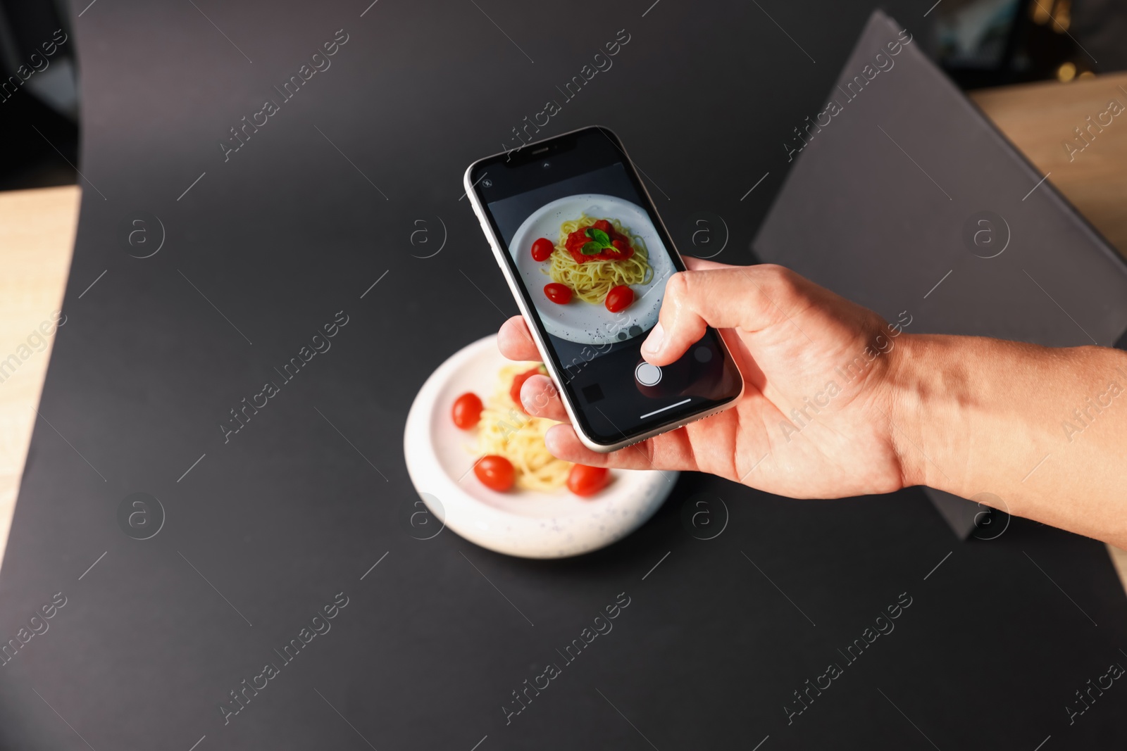 Photo of Man taking picture of pasta with smartphone in studio, closeup. Professional food photography