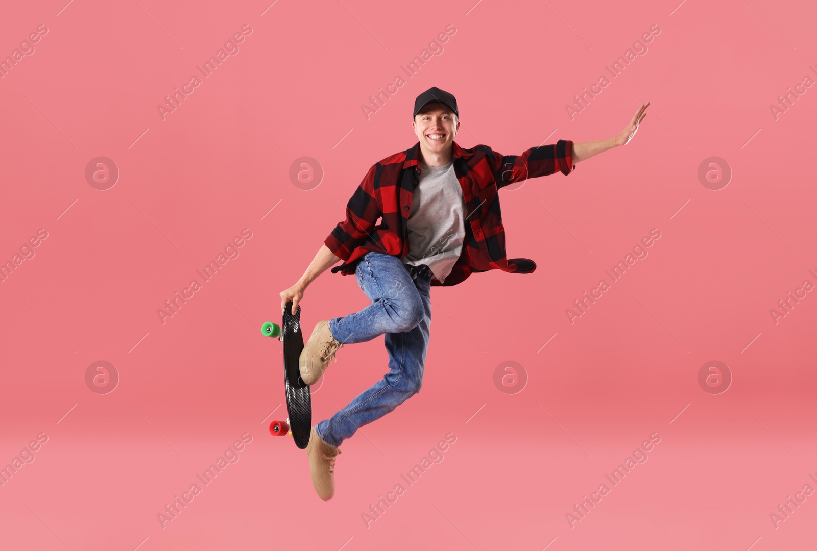 Happy young man with penny board jumping on pink background Photo of Happy young man with penny board jumping on pink background