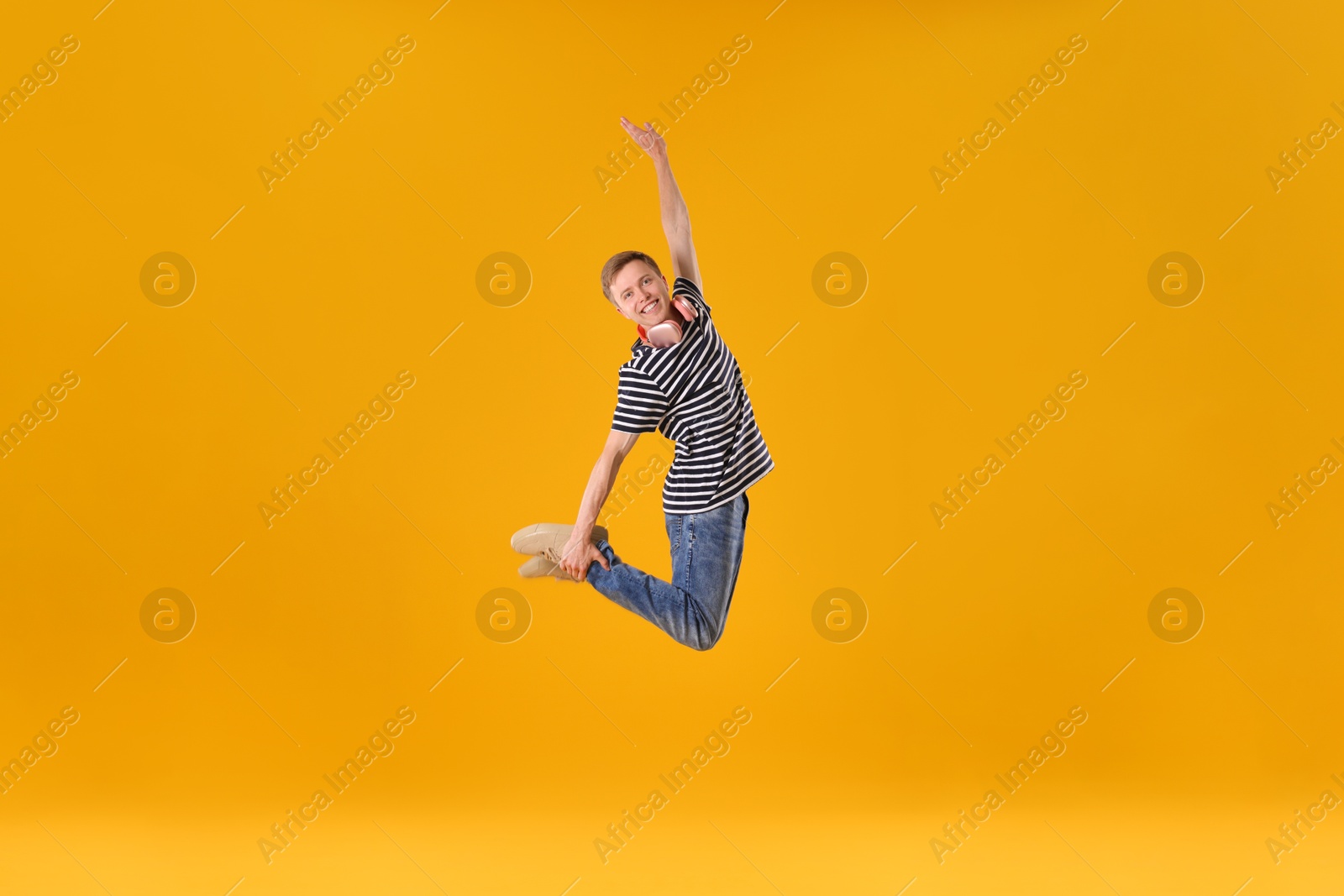 Happy young man with headphones jumping on orange background Photo of Happy young man with headphones jumping on orange background