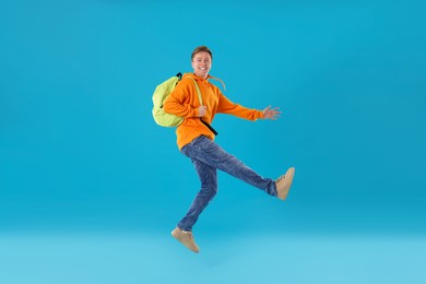 Photo of Happy young man with backpack jumping on light blue background