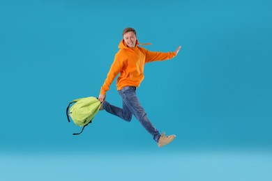 Photo of Happy young man with backpack jumping on light blue background