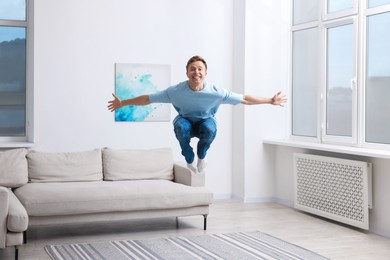Photo of Portrait of happy young man jumping at home