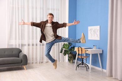 Photo of Portrait of happy young man jumping at home