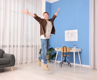 Photo of Portrait of happy young man jumping at home
