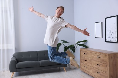 Photo of Portrait of happy young man jumping at home
