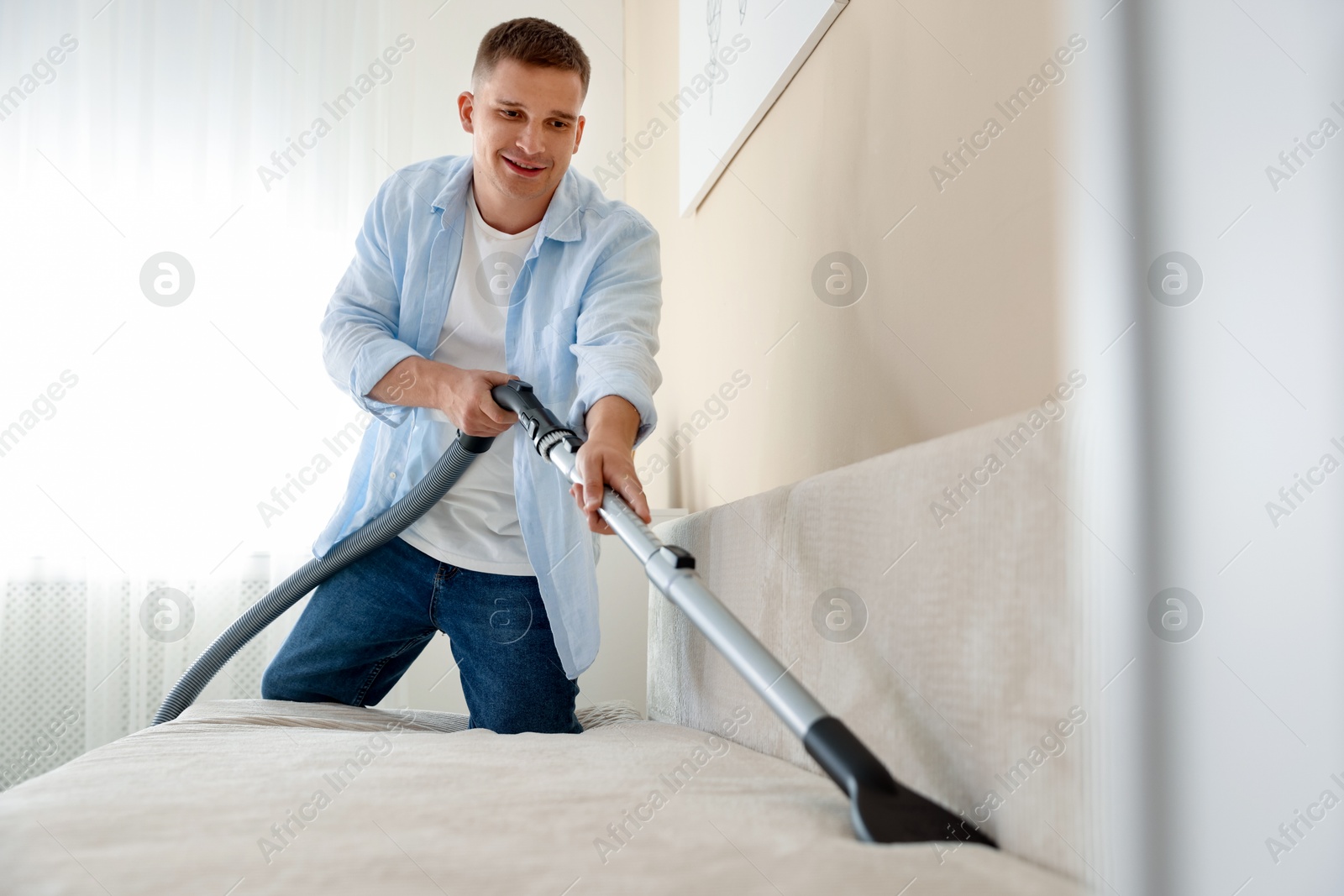 Man cleaning sofa with vacuum cleaner at home Photo of Man cleaning sofa with vacuum cleaner at home