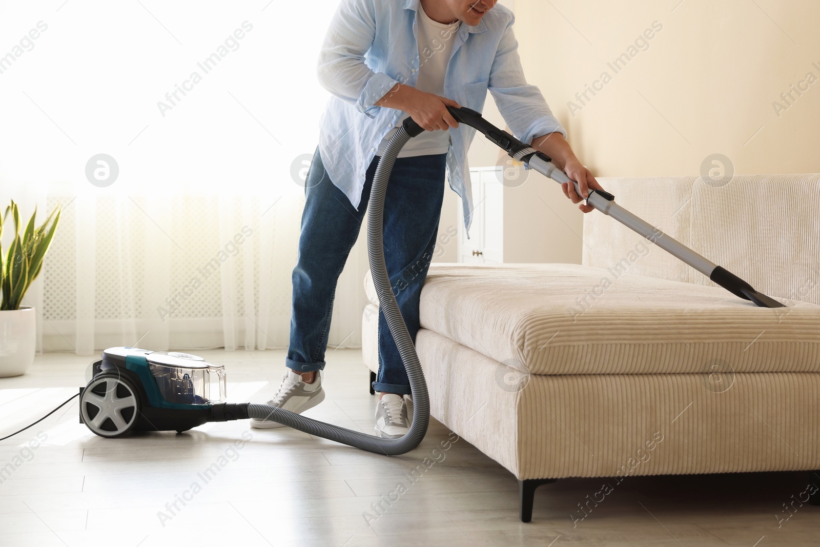 Man cleaning sofa with vacuum cleaner at home, closeup Photo of Man cleaning sofa with vacuum cleaner at home, closeup