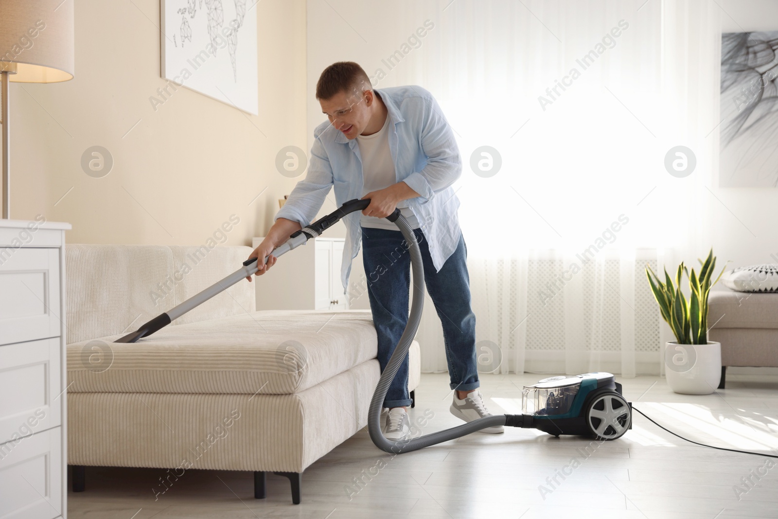 Man cleaning sofa with vacuum cleaner at home Photo of Man cleaning sofa with vacuum cleaner at home