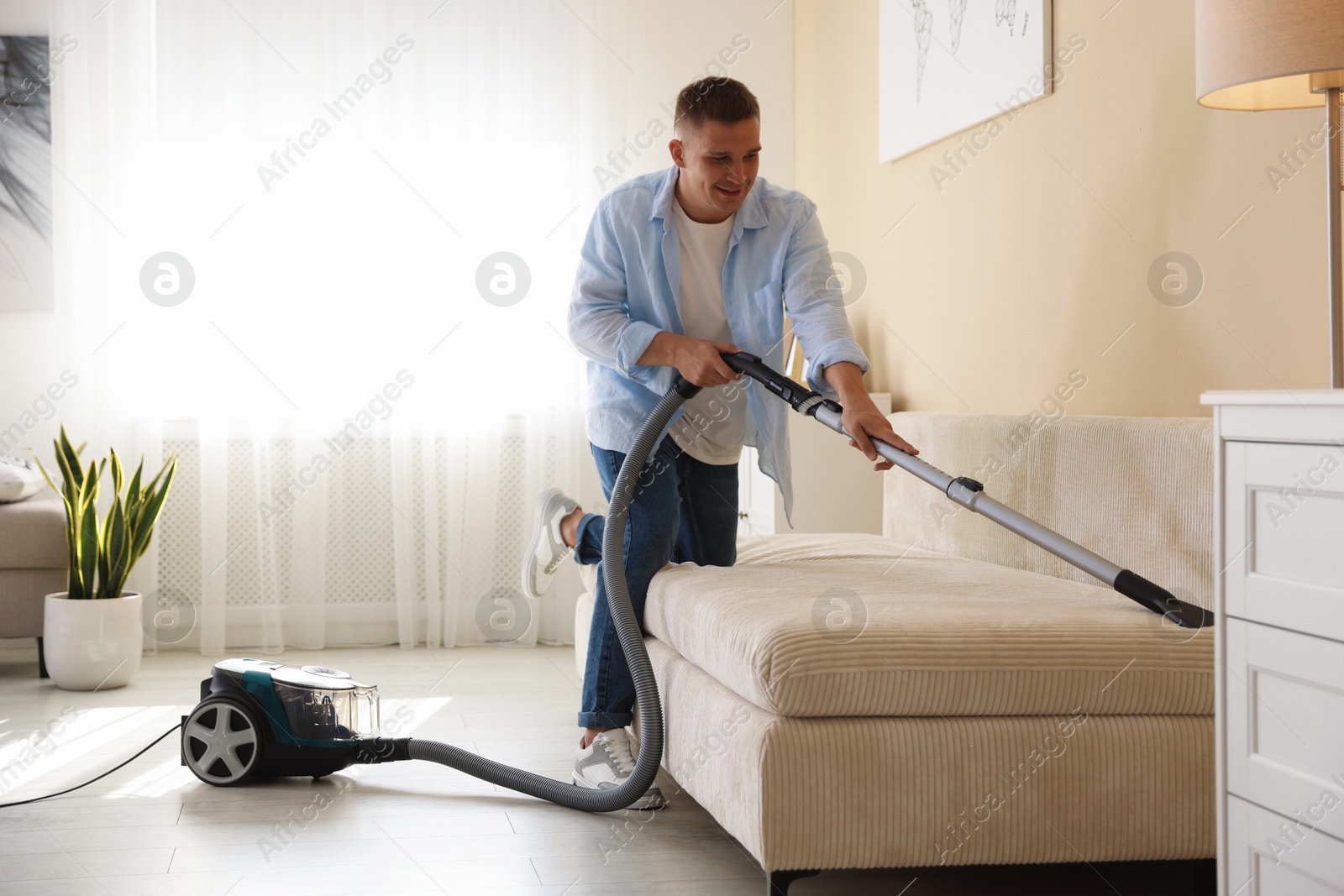 Man cleaning sofa with vacuum cleaner at home Photo of Man cleaning sofa with vacuum cleaner at home