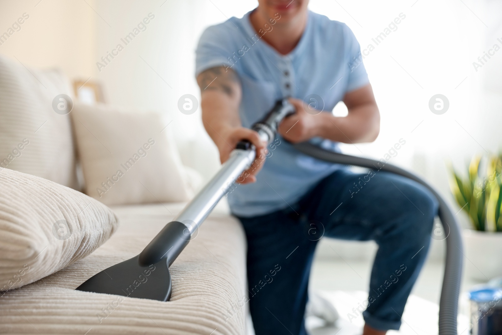 Man cleaning sofa with vacuum cleaner at home, selective focus Photo of Man cleaning sofa with vacuum cleaner at home, selective focus