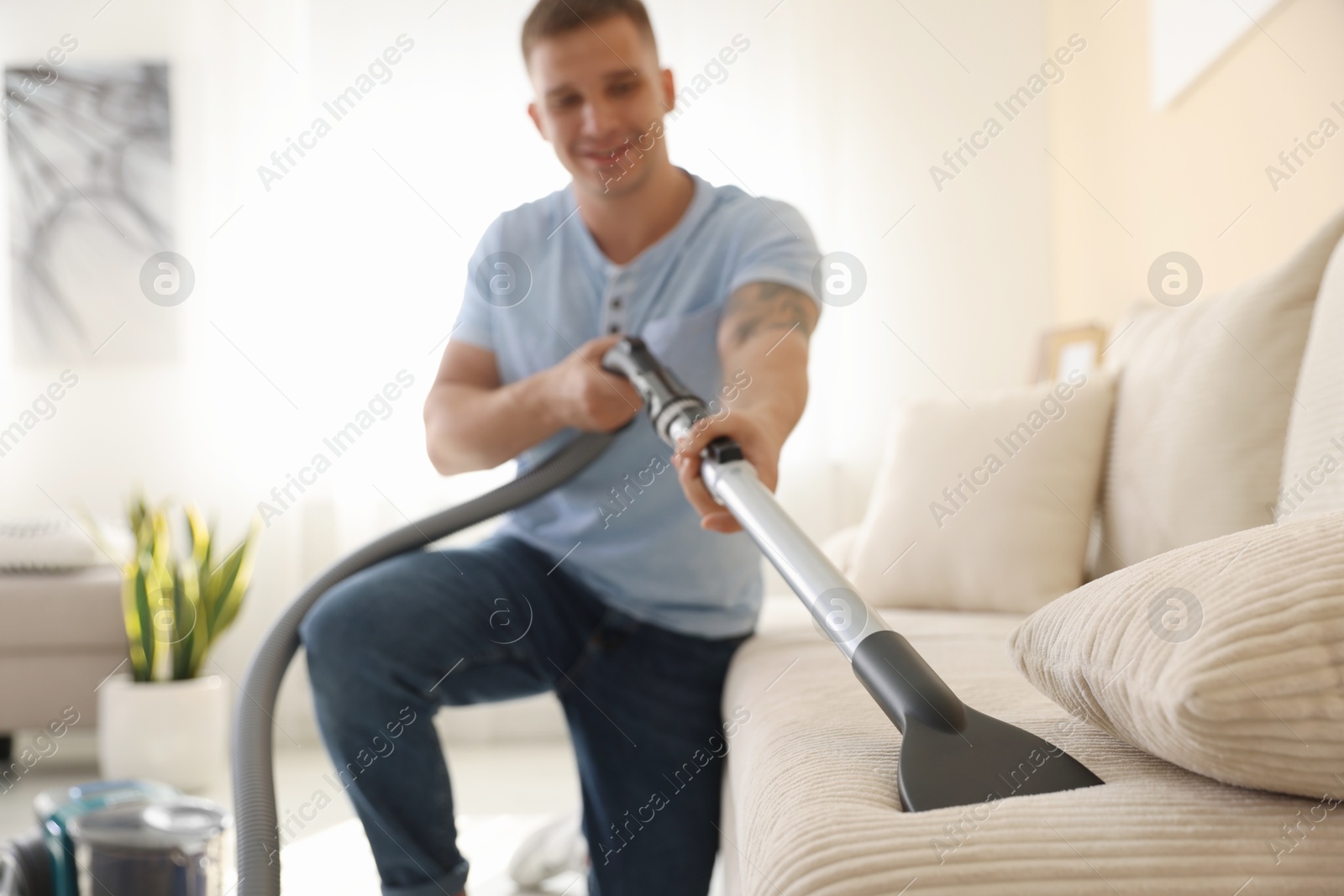 Man cleaning sofa with vacuum cleaner at home, selective focus Photo of Man cleaning sofa with vacuum cleaner at home, selective focus