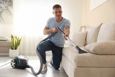 Photo of Man cleaning sofa with vacuum cleaner at home
