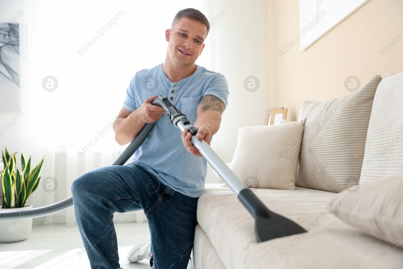 Man cleaning sofa with vacuum cleaner at home Photo of Man cleaning sofa with vacuum cleaner at home