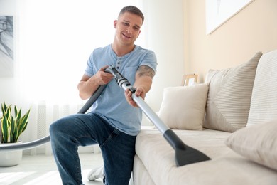 Photo of Man cleaning sofa with vacuum cleaner at home