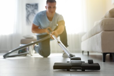 Photo of Man cleaning floor with vacuum cleaner at home, selective focus