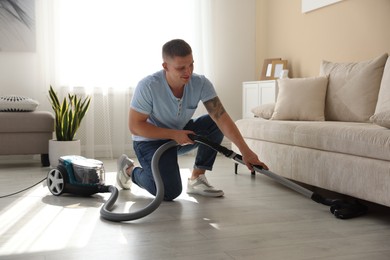 Photo of Man cleaning floor with vacuum cleaner at home
